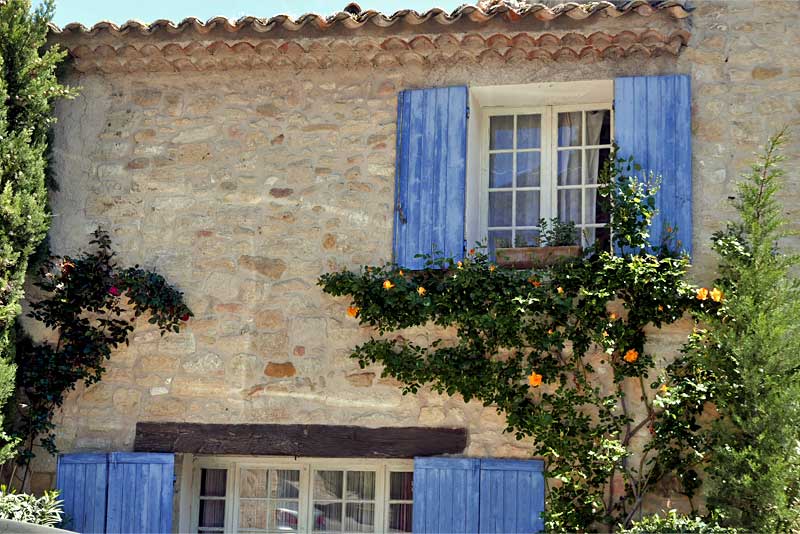 プロヴァンス・リュベロン地方の村Ansouisにある建物。ブルーのヴォレと美しいオレンジ色の花が壁を飾っている。